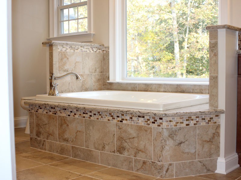 The tub area after a bathroom remodel featuring large tiled tub in front of a large window