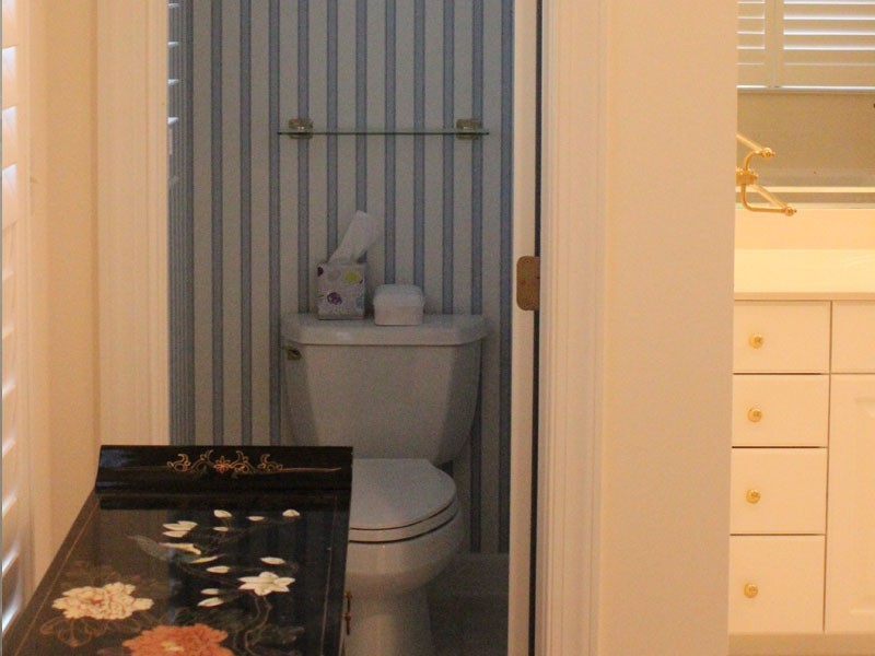 Bathroom before a remodel showing a dark enclosed toilet with blue and white striped wallpaper