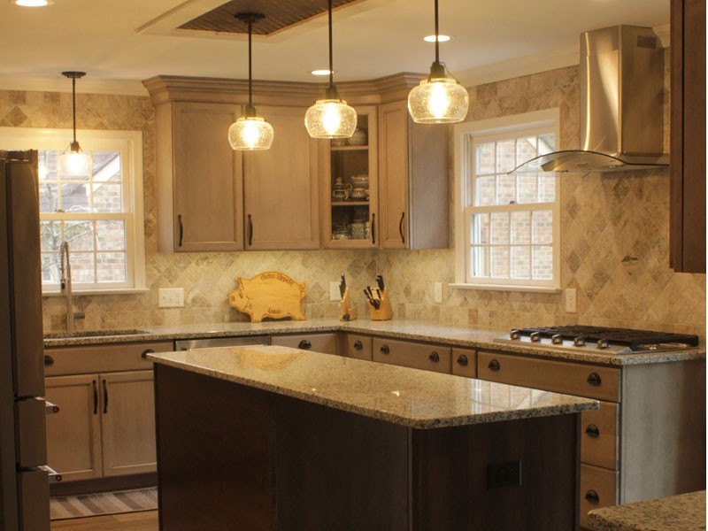 A finished kitchen remodel with pendant lighting over an island, light colored cabinets, and a modern stove vent over a cooktop